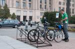 Minister Mateusz Szczurek w sportowym stroju stawia rower na stojaku na dziedzińcu ministerstwa.