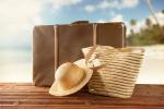 Zdjęcie ilustrujące akcję Przed wakacjami - co warto wiedzieć? (walizka, torba, kapelusz plażowy, w tle plaża z palmami)