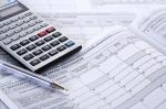 Które PIT-y składamy do 2 marca - grafika prezentująca kalkulator wraz długopisem na tle formularzy podatkowych.