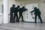 Uzbrojeni i zamaskowani ludzie stoją przed drzwiami wejściowymi do domu