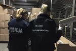 Na zdjęciu magazyn z pudłami z nielegalnymi papierosami, widoczne funkcjonariuszki Służby Celno-Skarbowej i Policji