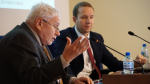 Profesor siedzi przy stole prezydialnym i przedstawia prezentację.