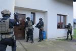 Na zdjęciu umundurowani i uzbrojeni funkcjonariusze przed drzwiami domu