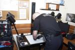 Funkcjonariusz podczas pracy przy badaniu śladów przestępstwa za pomocą specjalistycznego sprzętu.