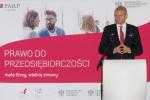Minister Paweł Gruza podczas wystąpienia, w tle napis PRAWO DO PRZEDSIĘBIORCZOŚCI, małe firmy, wielkie zmiany.