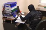 Funkcjonariusz KAS analizuje dokumenty, obok segregatory na biurku.